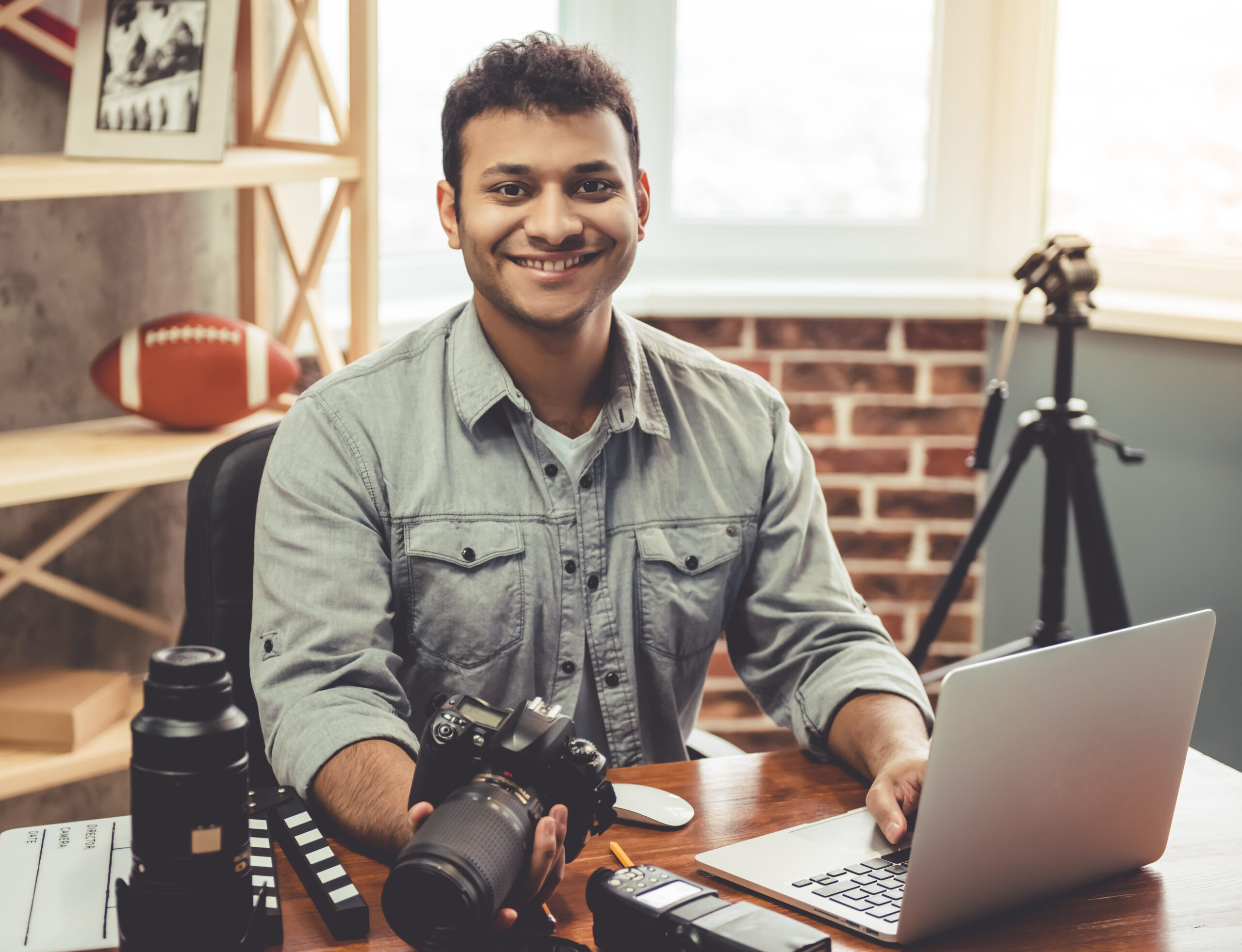 Afro American photographer is holding his camera and smiling while sitting in his office